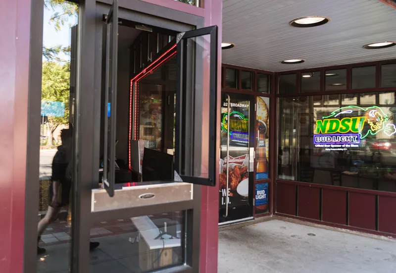 Exterior corner entrance of a bar or restaurant with NDSU Bud Light neon sign in window