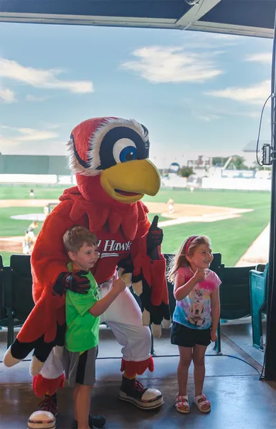 Red hawk mascot posing with two young children at a baseball stadium