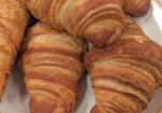 Several golden-brown baked croissants on a white plate