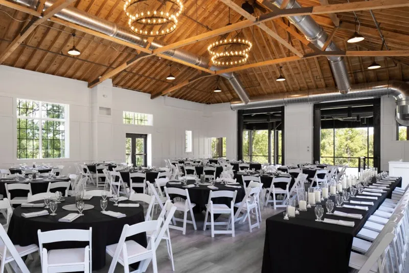 Banquet hall with vaulted wood ceiling, ring chandeliers, and black-linened tables set with white folding chairs