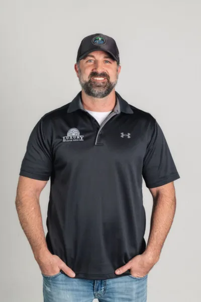 Bearded man in black Under Armour polo and cap smiling against gray background