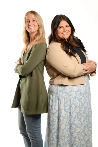Two smiling women standing back-to-back with arms crossed against a white background