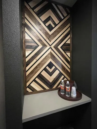Geometric wood wall art with dark and natural tones above a shelf holding two water bottles on a round tray