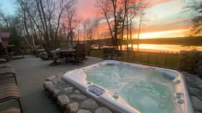 Bubbling hot tub on a lakeside patio at sunset with bare trees and glowing orange sky