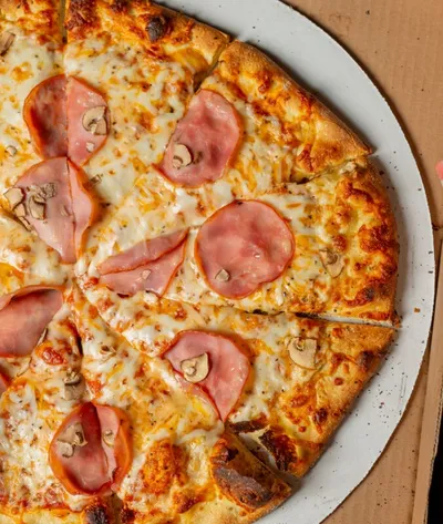 Sliced pizza topped with ham, mushrooms, and melted cheese on a metal pan