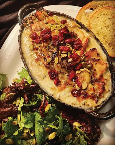 Baked cheese dip with roasted tomatoes and pumpkin seeds in a cast-iron dish, served with toasted bread and green salad