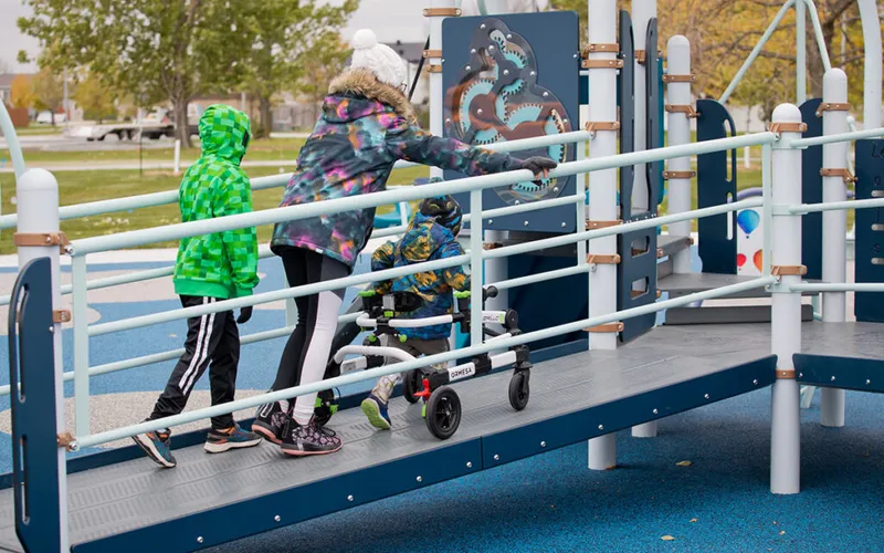 Two children and a child using a mobility walker on an accessible playground ramp