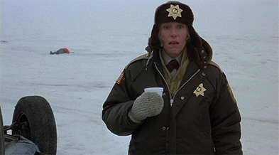 Actor in sheriff uniform and fur hat holding a cup in a snowy field