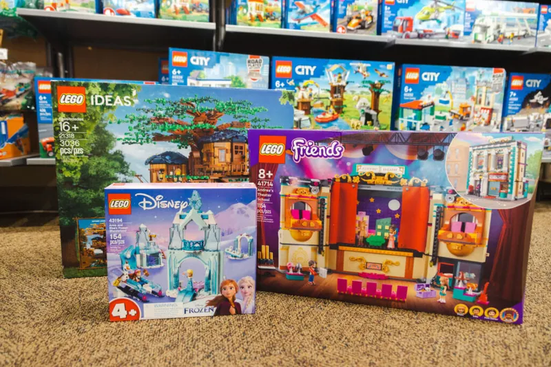Three LEGO sets displayed on carpet: LEGO Ideas Treehouse, Disney Frozen, and Friends Theater, with LEGO City boxes on