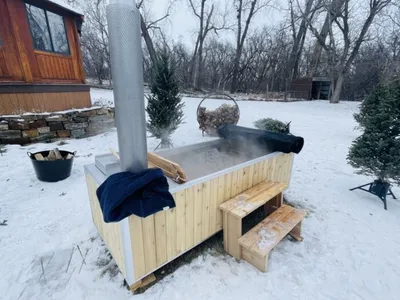 Wood-fired outdoor hot tub with metal chimney steaming in a snowy backyard