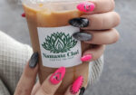 Hand with pink floral nails holding an iced coffee in a branded cup