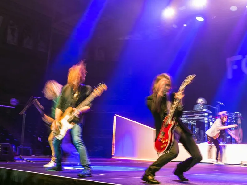 Two guitarists perform energetically on a blue-lit stage, motion blur capturing their movement