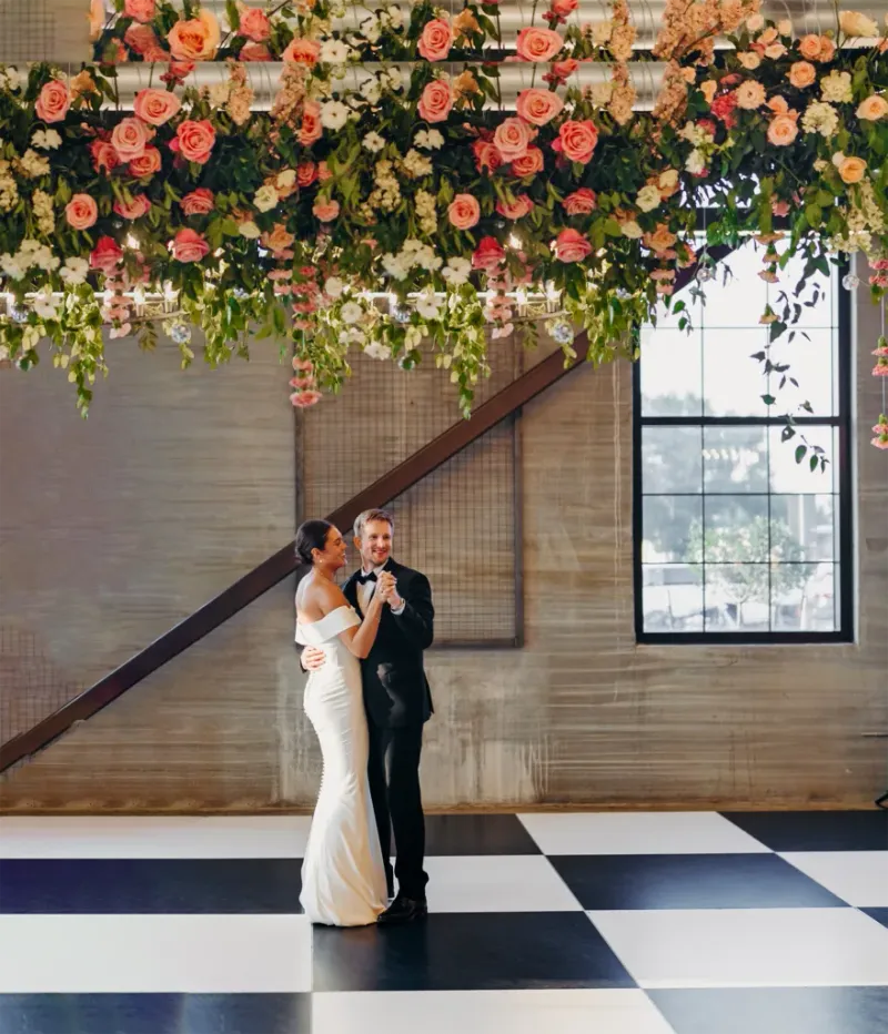 Couple shares first dance on checkered floor beneath lush hanging pink rose installation