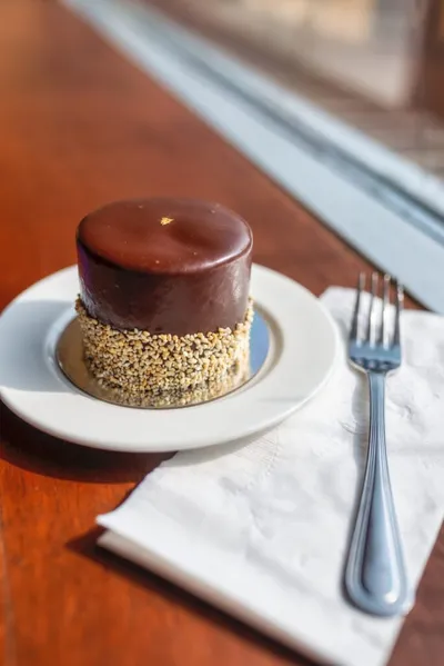 Small chocolate-glazed cake with chopped nut sides on a white plate with a fork