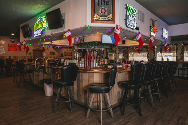 Wood-paneled bar with black stools, neon beer signs, and Christmas stockings strung with colorful lights