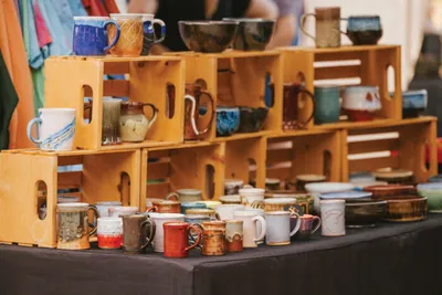 Colorful handmade ceramic mugs displayed on stacked wooden crate shelves at a market