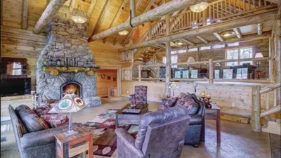 Rustic log cabin interior with stone fireplace and leather sofas under vaulted wood-beam ceiling
