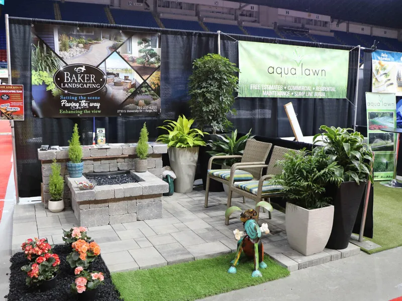 Landscaping trade show booth with a stone fire pit, potted plants, and a patio chair display
