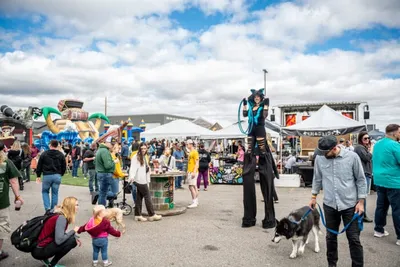Stilt walker in costume entertaining a crowd at an outdoor festival with vendor tents