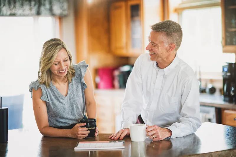 Man and woman smiling together over coffee mugs at a kitchen counter