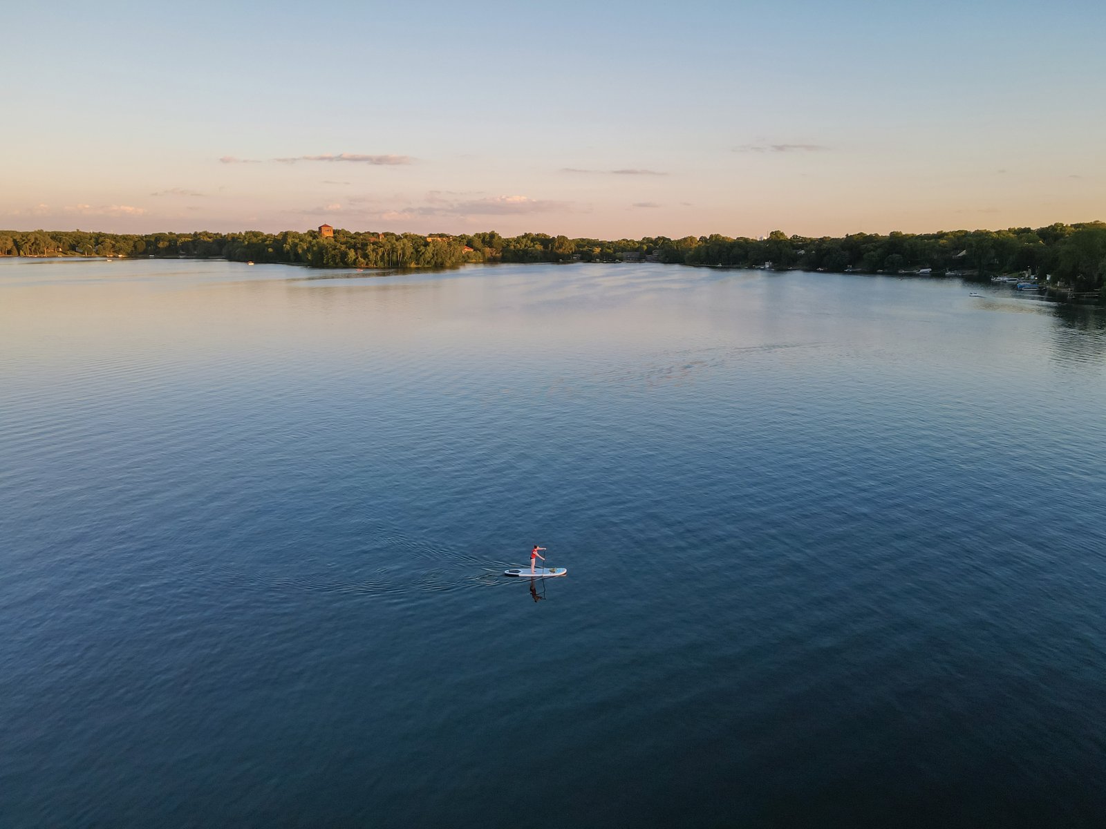 A paddleboarder glides across a calm lake at sunset