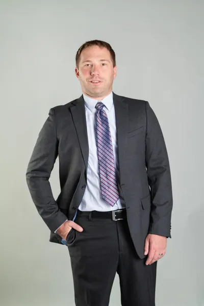 Man in dark gray suit and striped tie posing against a gray background