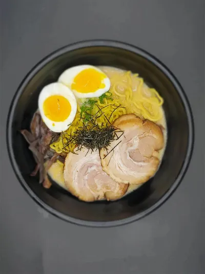Overhead view of tonkotsu ramen topped with chashu pork, soft-boiled egg, nori, and bamboo shoots in a dark bowl