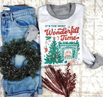 Folded holiday graphic sweatshirt beside jeans, a small wreath, and red berry stems
