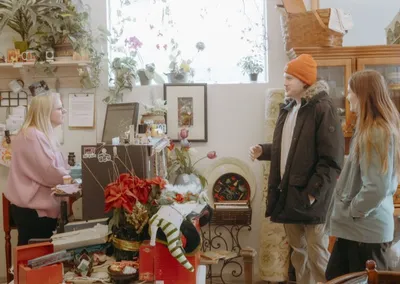 Two customers chat with a shop employee amid holiday décor and plants in a cozy consignment store