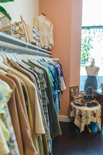 Colorful clothing rack in a boutique with a mannequin and floral-draped table in the background