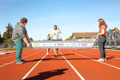 Man crossing a finish line tape held by two people on a red running track