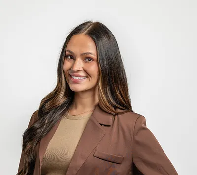 Smiling woman with long dark hair wearing a brown blazer over a tan top