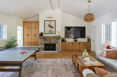 Bright living room with stone fireplace, wall-mounted TV, ping-pong table, and woven pendant light