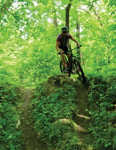 Mountain biker in helmet navigating a rocky drop on a wooded forest trail