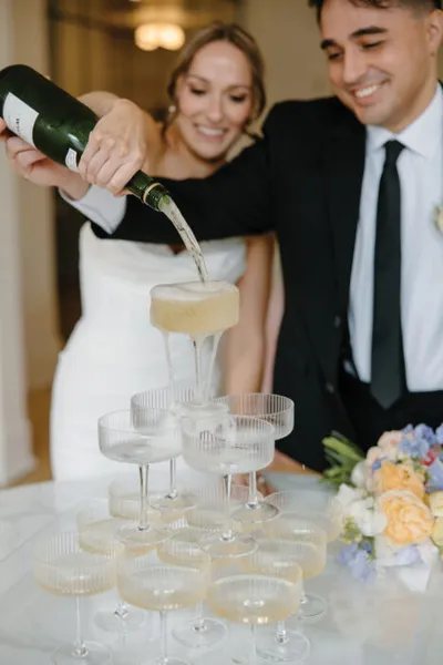 Smiling bride and groom pouring champagne over a tiered coupe glass tower