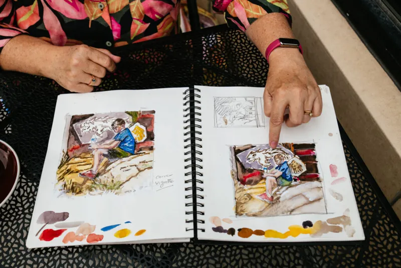 Woman pointing to watercolor sketches in an open spiral sketchbook with paint swatches on edges
