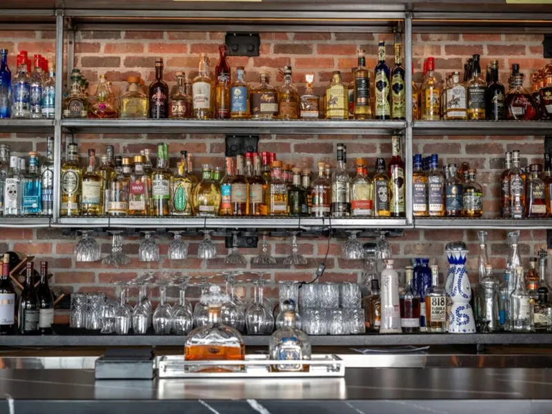 Bar shelves lined with tequila bottles against an exposed brick wall, with hanging stemware