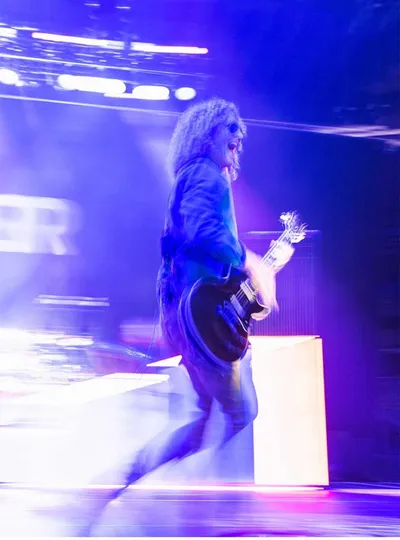 Long-haired guitarist performing on a fog-filled stage bathed in purple light