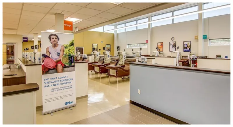 Bright medical infusion clinic interior with recliner chairs, IV stations, and a Shire promotional banner