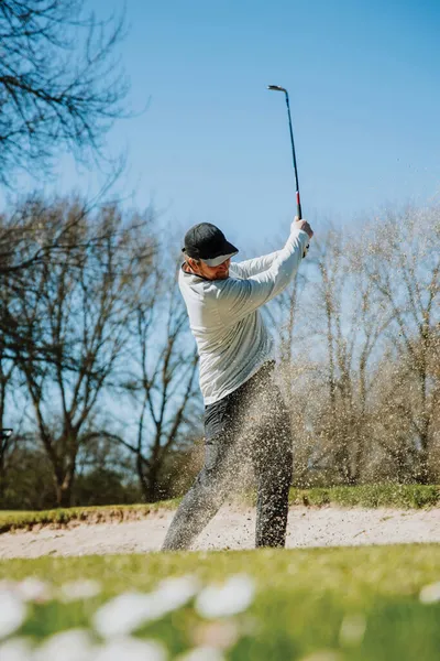 Golfer hitting a sand bunker shot with an explosion of sand mid-swing