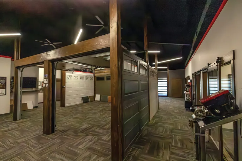 Indoor showroom displaying multiple garage door styles with wood beam framing and dark ceiling