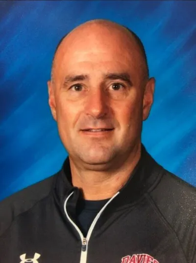 Bald man in a dark Under Armour quarter-zip smiling against a blue backdrop