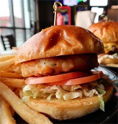 Crispy fish sandwich with tomato and shredded lettuce on a brioche bun, served with waffle fries