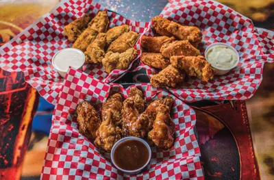 Three baskets of fried chicken wings with dipping sauces on red checkered paper