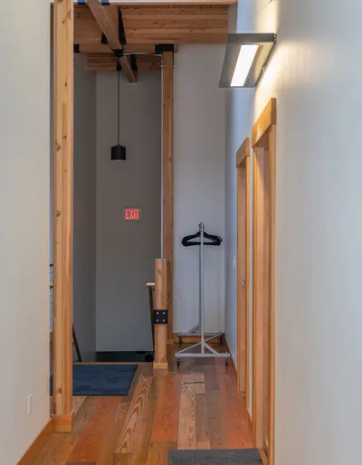 Narrow wood-floored hallway with pine trim, a rolling clothes rack, and a red exit sign