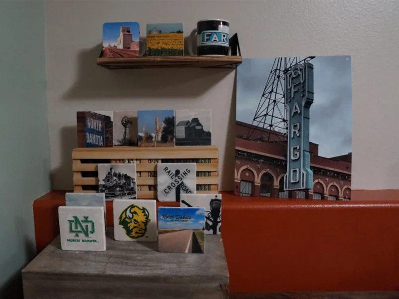 North Dakota-themed souvenirs and coasters displayed on a wooden shelf beside a Fargo theatre sign print