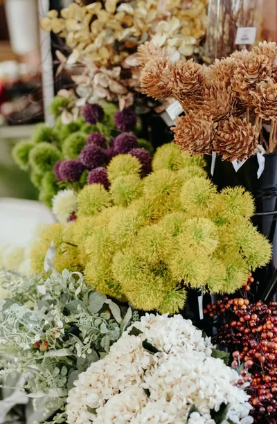 Colorful flower market display with green, purple, and dried blooms in buckets