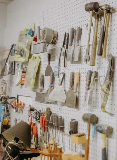 Pegboard wall hung with spatulas, hammers, chisels, and assorted hand tools in a workshop