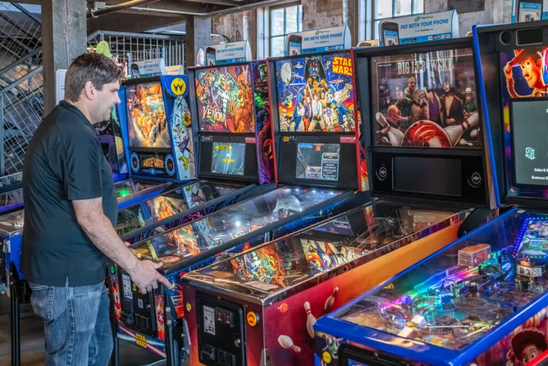 Man playing a Star Wars pinball machine in an arcade filled with themed machines