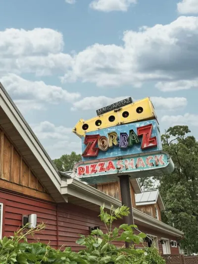 Colorful vintage neon sign for Zorbaz Pizza Shack above a red wooden building